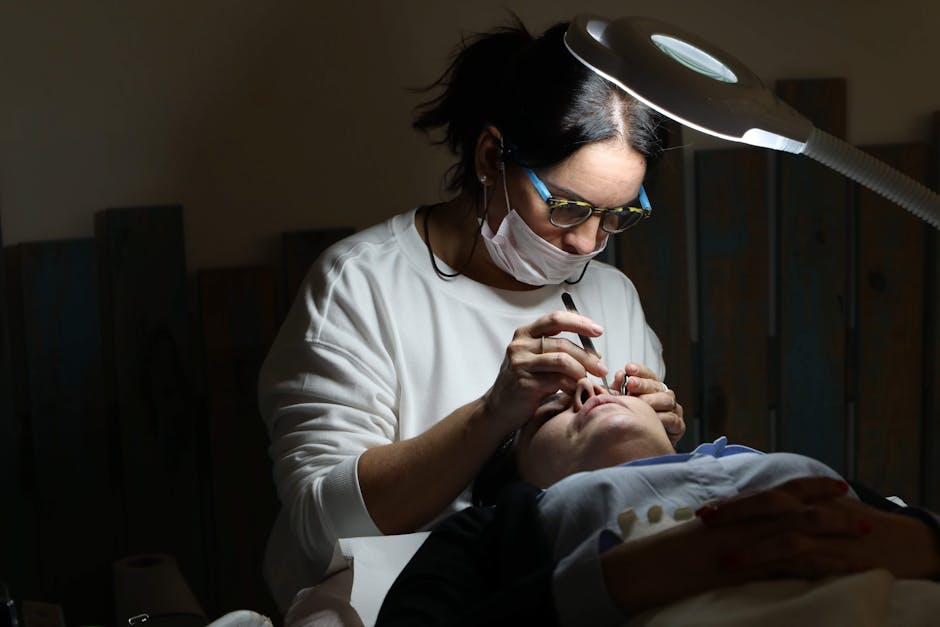 Professional cosmetologist applying eyelash extensions in a salon setting under focused lighting.