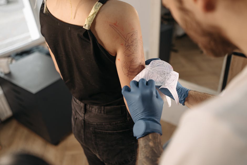 Tattoo artist applying a stencil to a client's arm inside a studio setting.