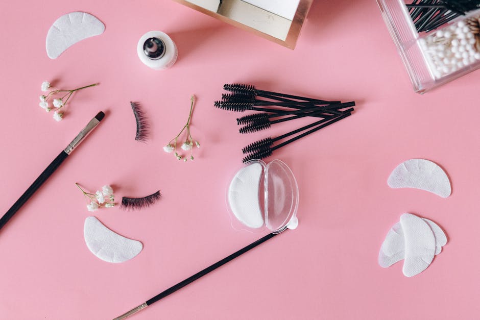 Aesthetic makeup tools and beauty items arranged on a pink surface.